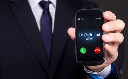 Businessman holding up a smartphone displaying an incoming call from his ex-girlfriend, indicating potential infidelity.
